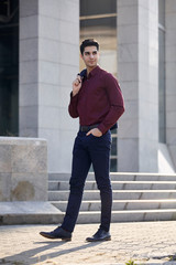 one young handsome man smirking, looking sideways, wearing suit, casually walking on pavement. modern building out of focus behind.