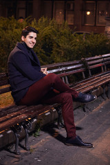 one handsome young man, 20-29 years old, posing, autumn clothes, sitting bench on city square. night time, dark.