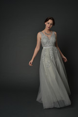 Fototapeta premium full length portrait of brunette girl wearing long silver ball gown. standing pose on grey studio background.