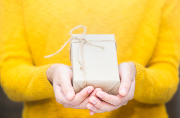 Young woman in yellow sweater holding gift box for spacial event.