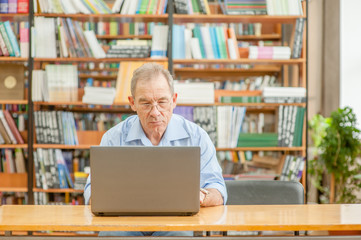 Senior man using laptop in library. Empty space for text