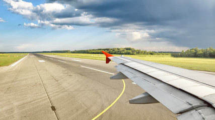 Fototapeta na wymiar passenger airplane window seat wing view on airport runway with dramatic clouds at blue summer sky air travel panoramic transportation landscape background