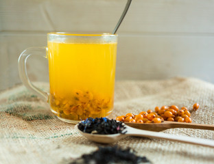 Vitaminic healthy sea buckthorn tea in small cup with fresh raw sea buckthorn berries and black tea in wooden spoons over sackcloth background. warm winter  organic drink, health food concept 