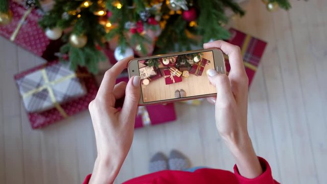 Beautiful woman photographing on smartphone christmas tree with new year gifts at home. X-mas, winter holidays and people concept. Shot from the first person. 4k uhd.