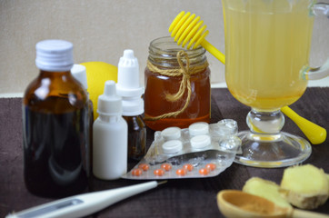 healthcare, traditional medicine and flu concept - tea cup with lemon, ginger, honey and pills on wooden table. tablets, pills, cough syrups, nasal drops and non-traditional alternative medicine.