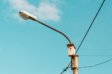Lamppost with wooden birdhouse. Wires for electricity in the lantern. Blue sky