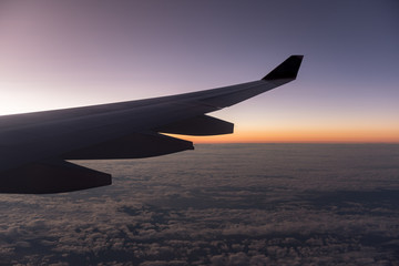 Fototapeta premium View from the window of airplane wing while fly over the blue sky with sea of clouds in twilight time.