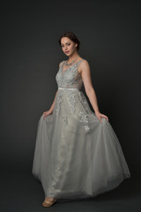 Fototapeta premium full length portrait of brunette girl wearing long silver ball gown. standing pose on grey studio background.