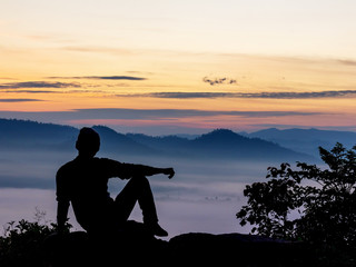 Young man sitting on mountain watching the sunrise at winter morning. Thinking and relaxing concept.