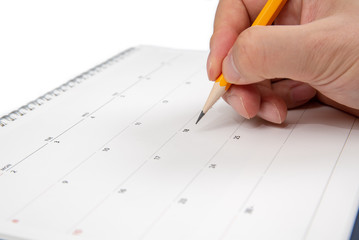 A man's hand holding a pencil in his hand and writing on a calendar.