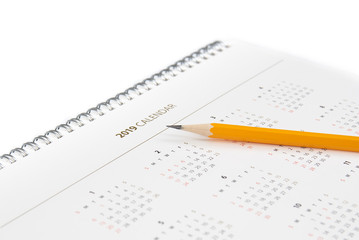 Desk calendar and yellow pencil on white background.