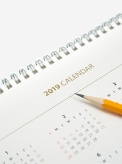 Desk calendar and yellow pencil on white background.