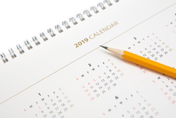 Desk calendar and yellow pencil on white background.