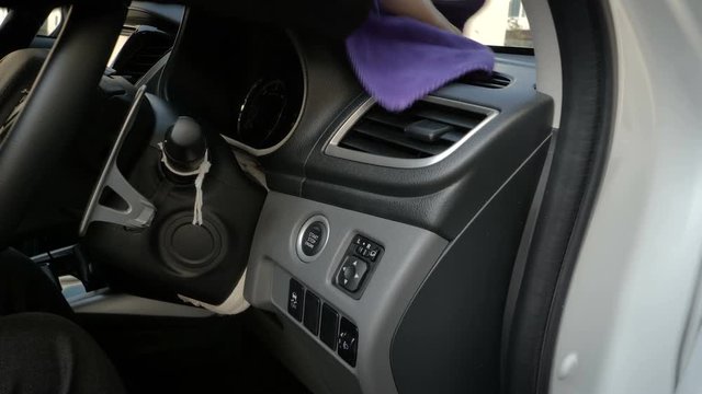Close up shot hand of woman using purple micro fiber fabric to clean interior of suv car front panel
