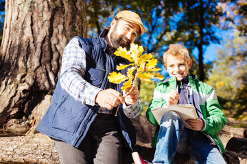 Oak leaves. Joyful positive man holding a tree branch while showing it to a boy