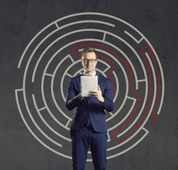 Businessman with computer tablet standing on a labyrinth background. Business, strategy, concept.