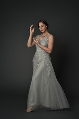 full length portrait of brunette  girl wearing long silver ball gown. standing pose on grey studio background. © faestock