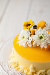 Fototapeta na wymiar Glazed Mango cheesecake with flowers and fresh mango pieces on grey background , vertical composition, close up