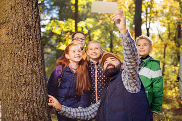 Now smile. Nice bearded man holding a digital device while taking photos with children
