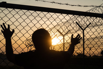 Silhouette of a prisoner behind a barbed wire fence steel jail  with the sunset in the background