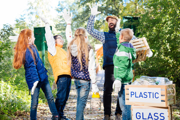 Environmental team. Happy delighted children giving high five to each other while cleaning the garbage