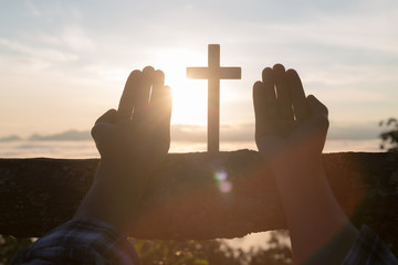 Silhouette of young  human hands praying with a  cross at sunrise, Christian Religion concept...