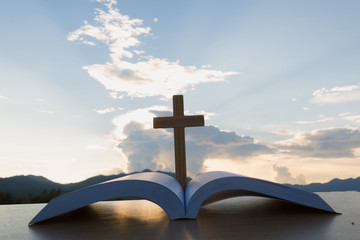 The wooden cross over opened bible on wooden table, Beautiful sky background