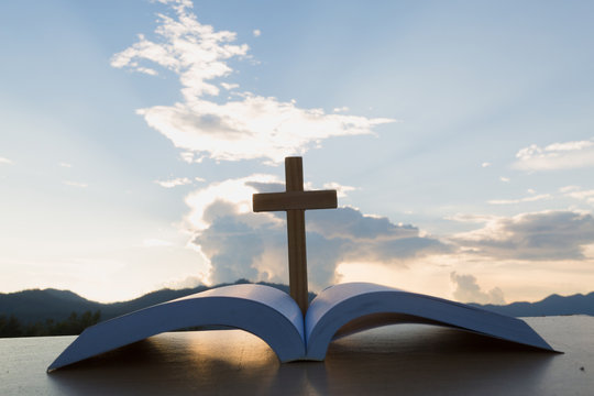 The wooden cross over opened bible on wooden table, Beautiful sky background