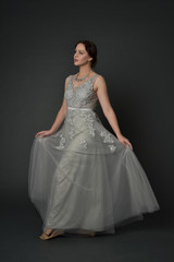Fototapeta premium full length portrait of brunette girl wearing long silver ball gown. standing pose on grey studio background.
