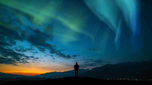 The man standing on a mountain against a sunrise and northern light. time lapse