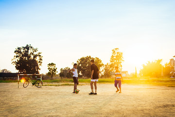 An action sport picture of a group of kids playing soccer football for exercise in community rural area under the sunset.