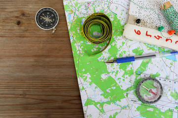 Top view of topographic map for orienteering or rogaining sport, compass and other accessories on brown wooden background with copy space for text.