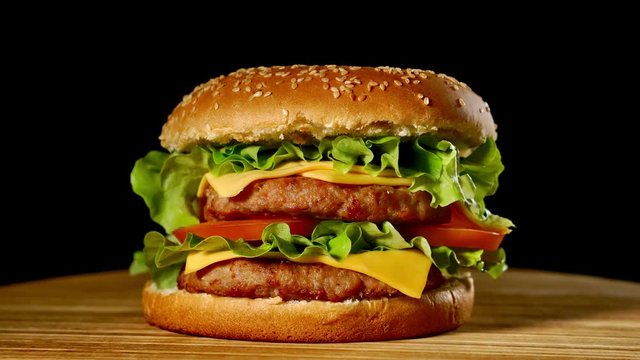 Fresh appetizing hamburger rotating on black background. Seamless loopable shot, 4k.