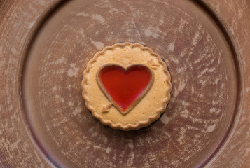 Cookies with red heart-shaped filling on dark brown plate for St. Valentine's Day. Top view