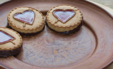 Gingerbread cookies with a red heart form filling on left side dark brown plate. Background for greeting card Valentine's day. Valentine day's present, sweet treat.