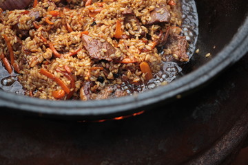 Pilaf prepare in big black cast iron with chefs hand. National cuisine concept.