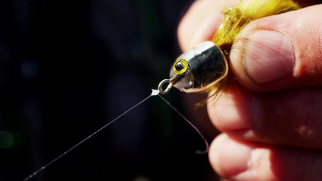 Hobby fisherman hand tying dry fly by freshwater river outdoor
