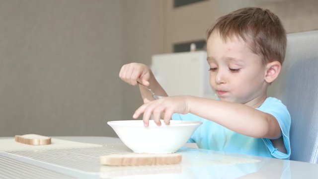 The child sits at the kitchen table and eats soup with bread with pleasure. The concept of healthy baby food.