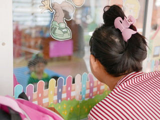 Asian mother eagerly looking at her baby through a window while come to fetch her daughter at a...