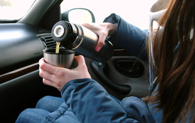 Close-up woman's hands pouring a hot tea in a cup from thermos in the car in winter.