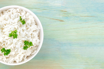 A closeup photo of a bowl of cooked white long rice, shot from above on a teal blue background with a place for text