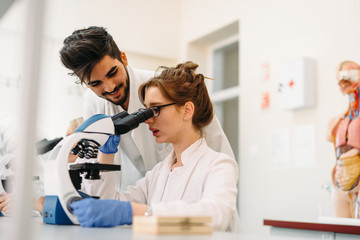 Fototapeta premium Young scientist looking through microscope in laboratory