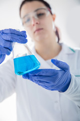 Chemist holding flask with blue liquid. Vertical view