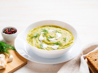 large white bowl with vegetable green cream soup of broccoli, zucchini, green peas on white background, side view