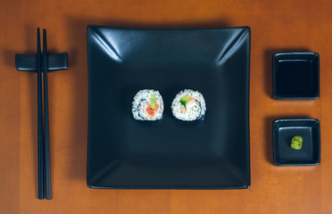 Sushi maki rolls presented on a plate with sauces and chopsticks