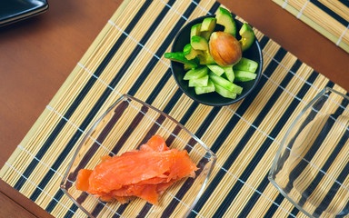 Top view of bowls with avocado, cucumber and salmon cut ready to prepare sushi