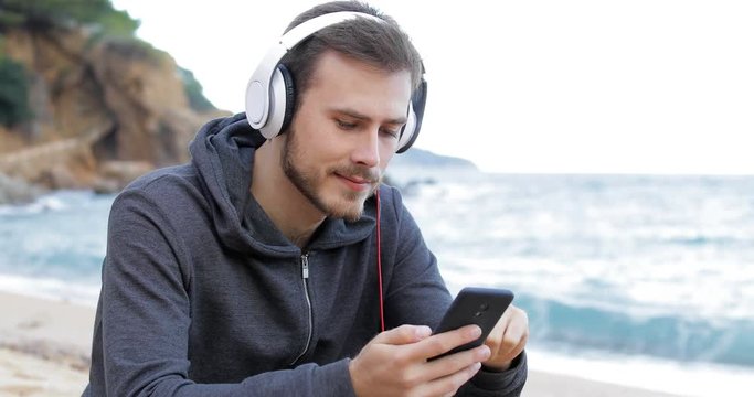 Serious teenage boy downloading and listening to music from a smart phone on the beach