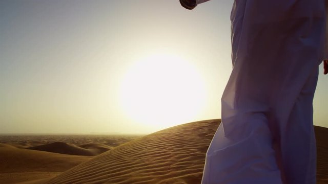 Proud Arab in dishdasha in silhouette at sunrise with his trained falcon