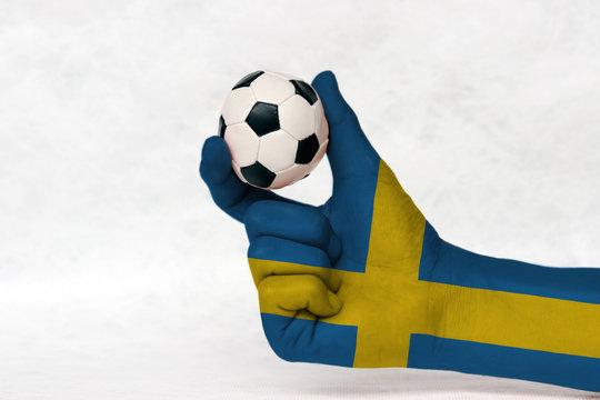 Mini ball of football in Sweden flag painted hand, hold it with two finger on white background. Concept of sport or the game in handle or minor matter.