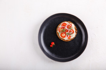 Whole grain bread sandwich with tomatoes and onion, seasoned with black pepper on black plate.
